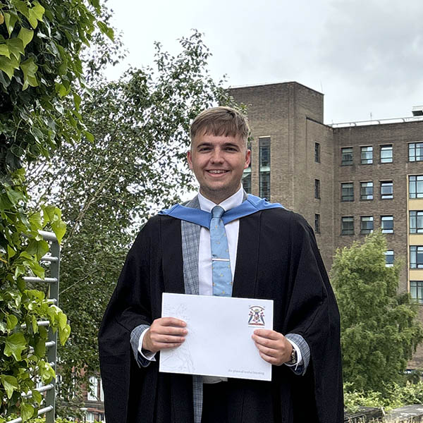 Jonathan Sneddon wearing graduation gown and holding degree certificate.